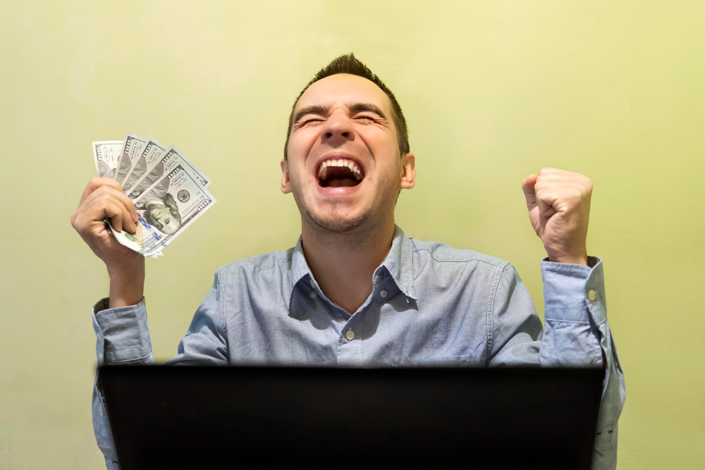 homme contant devant son ordinateur avec des billets dans ses mains
