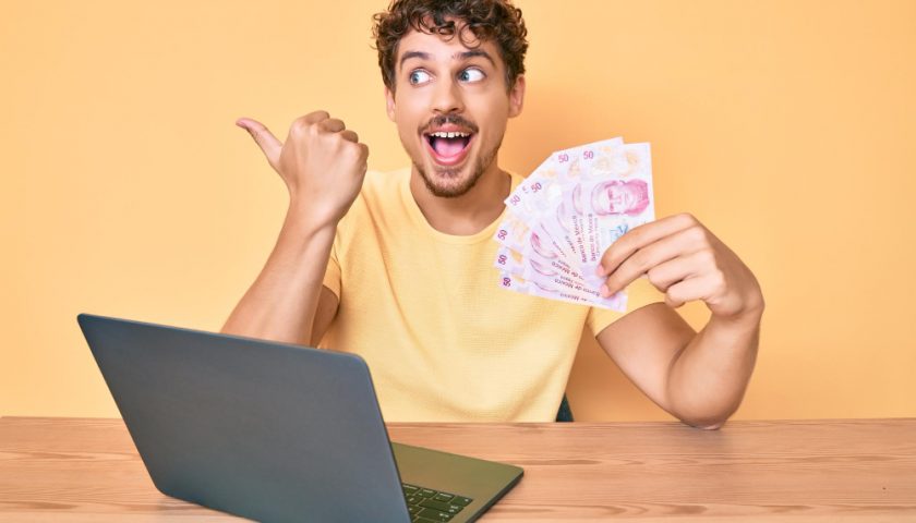 home levant le pouce devant son ordinateur avec des billets dans ses mains