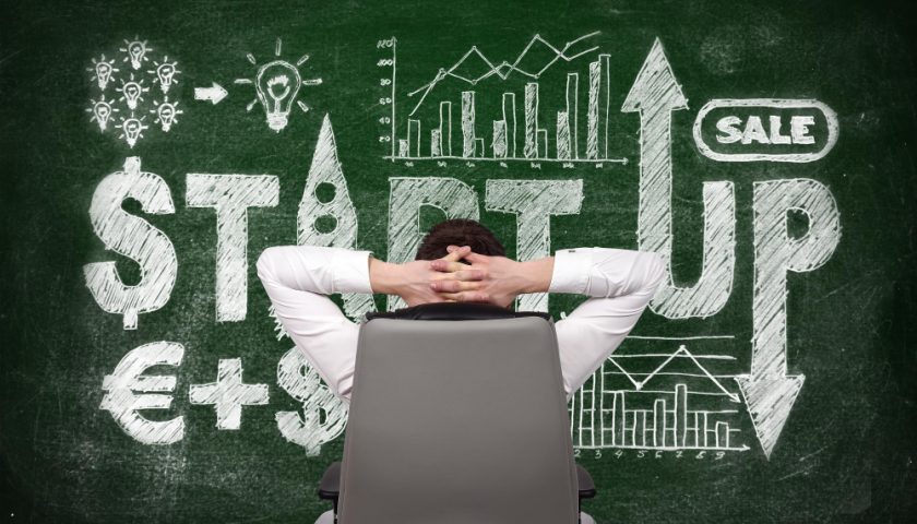 un homme les mains croisé assis devant un tableau de start up