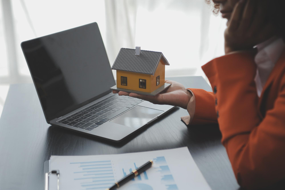 une personne tient une maison devant un ordinateur