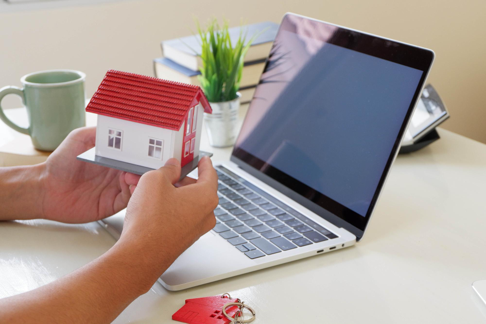 une personne tient une maquette de maison devant un ordinateur