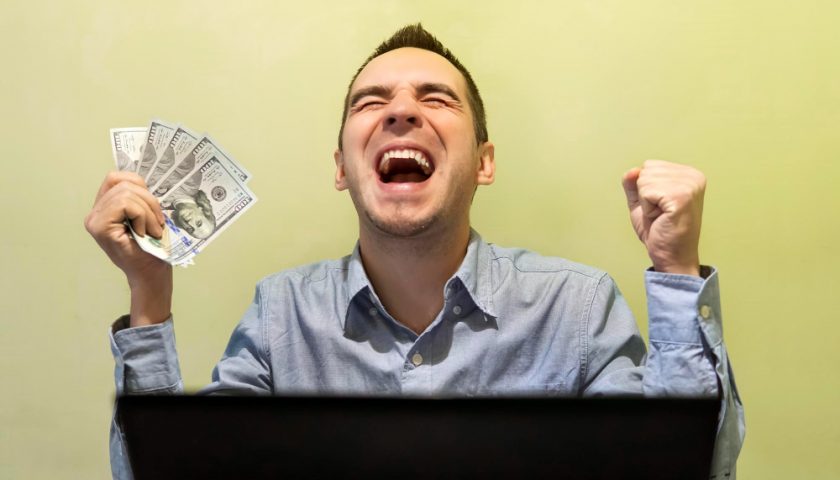 homme contant devant son ordinateur avec des billets dans ses mains